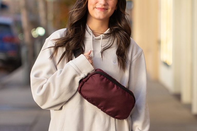 Woman in a hoodie looking straight ahead, one hand holding a red crossbody bag