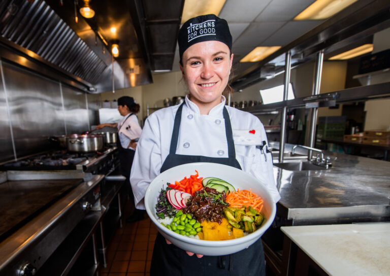 Chef trainee at employment social enterprise Kitchens for Good holds out a bowl of fresh food