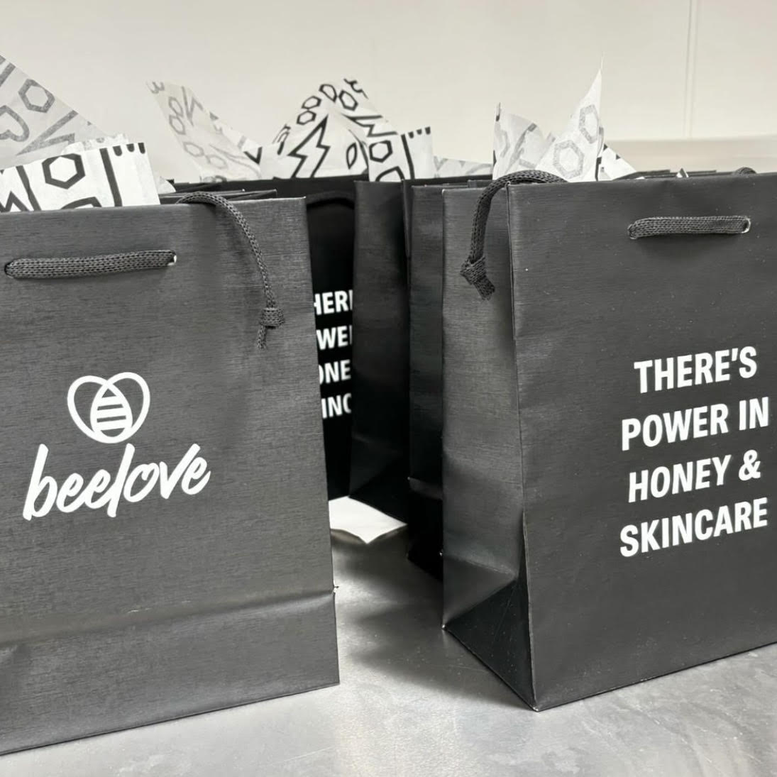 A set of black gift bags featuring NLEN's Beelove brand logo and slogan, "There's power in honey and skincare."